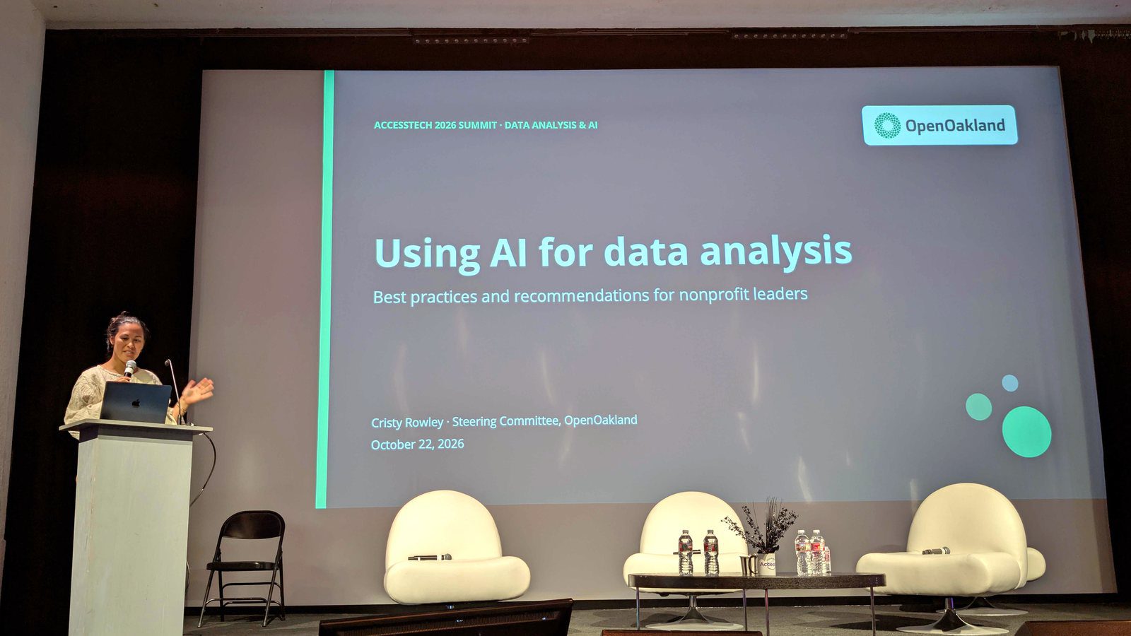 Cristy Rowley presenting at a podium beside a large screen showing the slide "Using AI for data analysis: Best practices and recommendations for nonprofit leaders" at the AccessTech 2026 Summit
